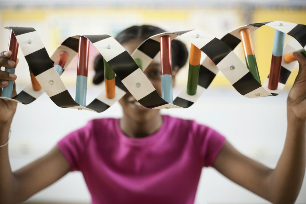A girl in a science class holding a model of a helix structure in front of her face.